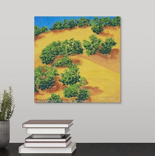 A painting of Lake Berryessa, CA golden hills filled with rows of green trees and their shadows hanging over a desk