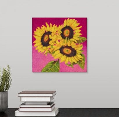 a painting by fine artist Nancy McLennon of a trio of yellow sunflowers and leaves on a fuchsia background over a desk