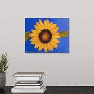 A painting of a Single sunflower & leaves on ultramarine blue background hanging over a black desk