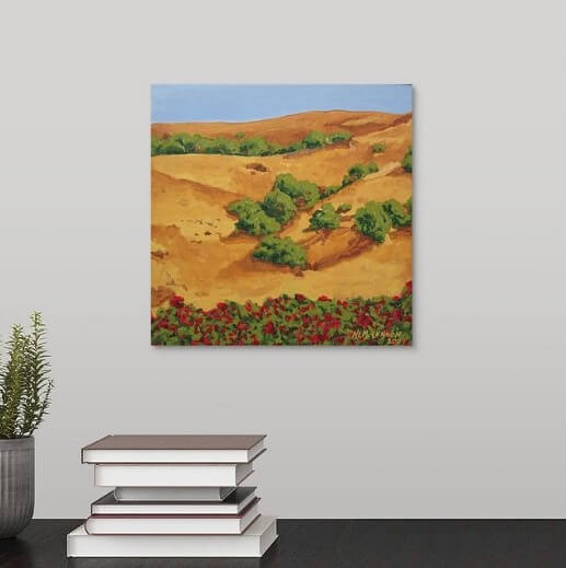 A painting of a sunburnt Sonoma, California hillside with yellow grasses, mixed with red roses and shrubbery, under a clear blue sky hanging over a black desk