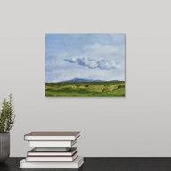 painting of a green springtime pasture in a Sonoma, California with rolling hills, billowing distant clouds, blue sky, and many piles of unwrapped hay laying in the abundant grasses hanging over a black desk
