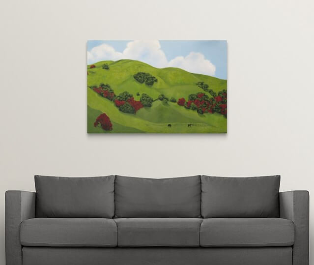 A landscape painting of lush green hillsides of Sonoma County, California in the winter rainy season. The painting includes dark green shrubs blooming with red flowers and two horses feeding on the green grass on a white wall over with a grey couch