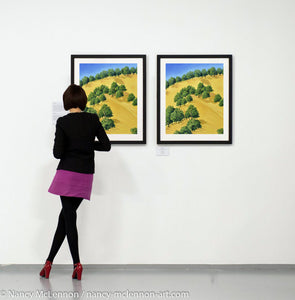Two Paintings of sunlit trees on the golden hillside that surrounding Lake Berryessa in the Napa Valley, California in summertime hanging on a gallery wall with art patron
