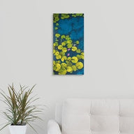 A Painting of a deep blue & aqua blue pond with floating golden yellow lily pads and purple flower blooms painting hanging over a couch