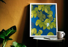 Load image into Gallery viewer, A deep blue &amp; aqua blue pond with floating golden yellow lily pads and white flower blooms painting leaning on a yellow wall